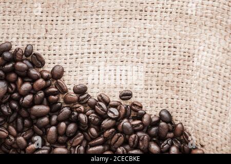 Les grains de café rôtis reposent sur le tissu du sac de jute. Plan à plat, photo d'arrière-plan de la vue de dessus Banque D'Images