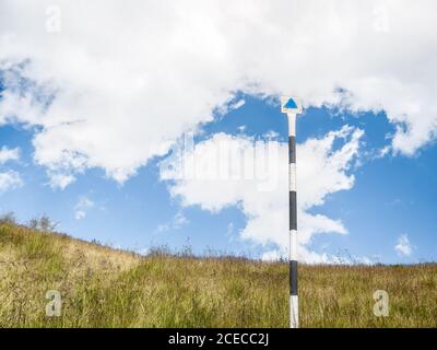 Triangle bleu de la piste de randonnée sur un poteau avec le ciel bleu et les nuages blancs en arrière-plan. Banque D'Images