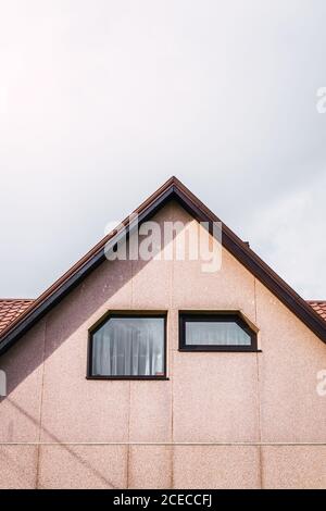 Deux fenêtres de forme inhabituelle situées sur le mur lumineux sous toit de maison moderne de campagne contre ciel nuageux Banque D'Images