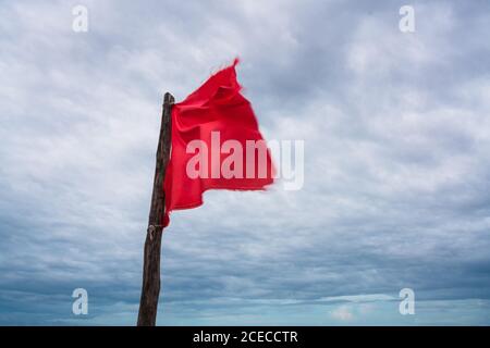 Bâton de bois avec pièce de tissu rouge ondulée sur vide plage de sable avec vagues de l'océan rugueuses en arrière-plan Banque D'Images