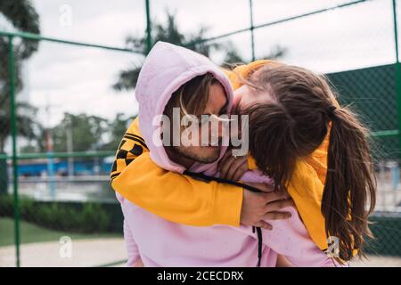 Un jeune gars sympa riant et donnant le pigeon à l'excitation petite amie tout en passant du temps sur le terrain de sport ensemble Banque D'Images