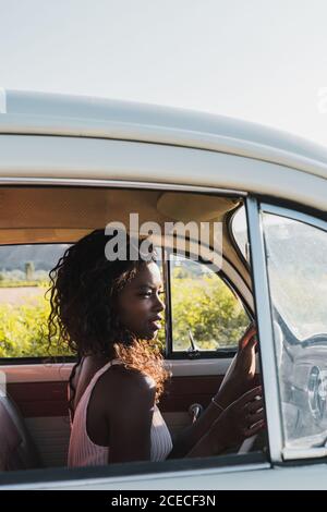 Les femmes multiethniques à la mode se tenant près d'une voiture d'époque et de la carte de lecture lors d'un voyage ensemble en été Banque D'Images