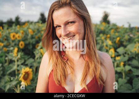 Portrait d'une femme blonde souriante avec des plantes de tournesol en arrière-plan pendant la saison de printemps Banque D'Images