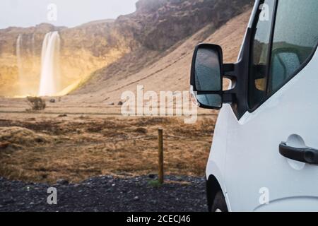 Fragment de récolte de véhicule blanc garé au sol avec vue sur les montagnes et la cascade en arrière-plan, Islande. Banque D'Images