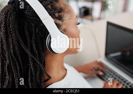 Jolie jeune femme avec des dreadlocks à l'écoute de la bonne musique dedans casque lorsque vous travaillez sur un ordinateur portable à la maison Banque D'Images