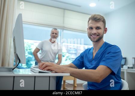 Jeune médecin souriant et patient âgé au bureau Banque D'Images