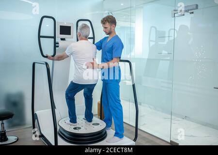 Homme âgé faisant de l'exercice sur simulateur spécial et médecin Banque D'Images