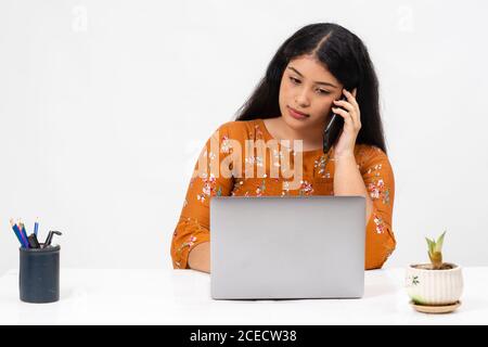 Jolie jeune femme indienne assise sur fond blanc et utilisant son ordinateur portable. Adorable adolescente faisant son travail scolaire en ligne de la maison. Banque D'Images