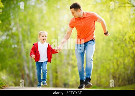 Père et fils courent sur la route dans le parc d'été. Concept de famille heureux Banque D'Images