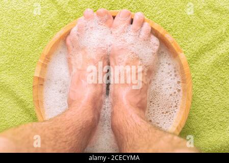 Pieds mâles dans un bol avec eau et savon, hygiène et concept spa Banque D'Images