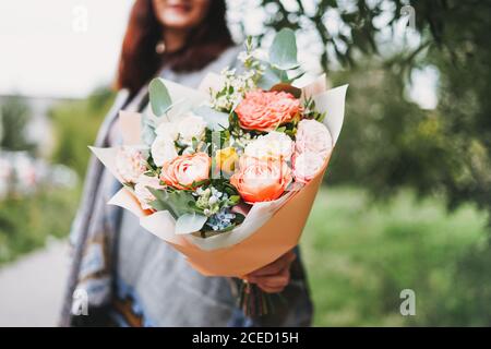 Jeune femme brune en poncho et jeans tient un beau bouquet de différentes fleurs Banque D'Images