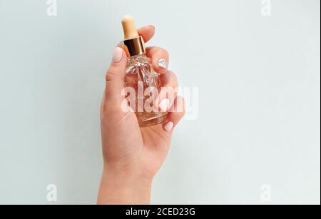 Vue de dessus de la femme anonyme avec des mains manucurées démontrant le blanc bouteille d'huile essentielle sur fond bleu clair Banque D'Images