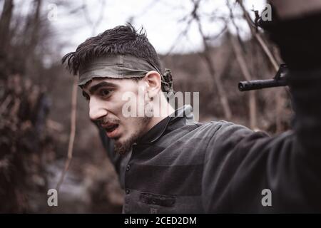 Membre révolutionnaire ou soldat homme dans la forêt avec un le fusil imposé sur sa tête lève ses mains d'otages et cessions Banque D'Images