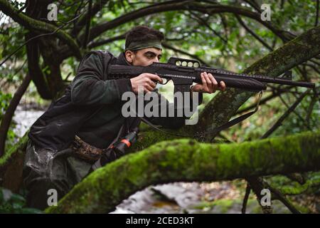 Soldat ou membre révolutionnaire ou chasseur visant avec le fusil dans sa main en camouflage dans la forêt, notion de chasse Banque D'Images