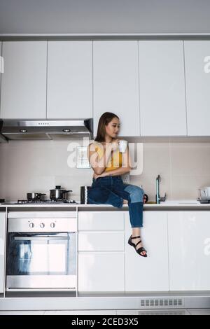 Jolie jeune femme asiatique assise et relaxante avec une tasse sur la table de cuisine à la maison. Banque D'Images