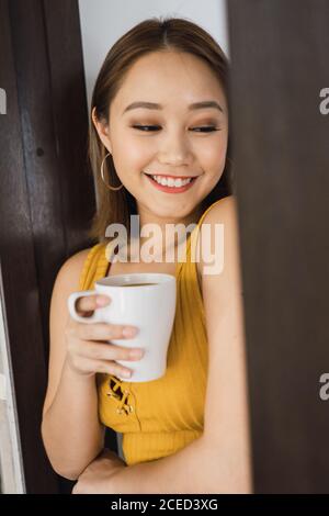 Jolie femme avec une tasse penchée sur le mur Banque D'Images