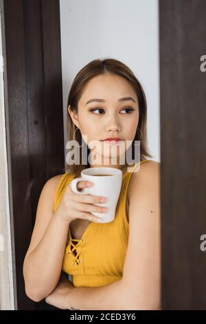 Jolie femme avec une tasse penchée sur le mur Banque D'Images