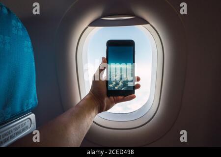 Rognez la main en tenant votre smartphone et en prenant des photos d'un blanc infini nuages derrière la fenêtre de l'avion Banque D'Images