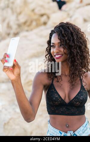 Jolie femme noire gaie utilisant le téléphone à l'extérieur Banque D'Images
