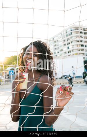 Magnifique femme noire avec une boisson derrière le filet Banque D'Images