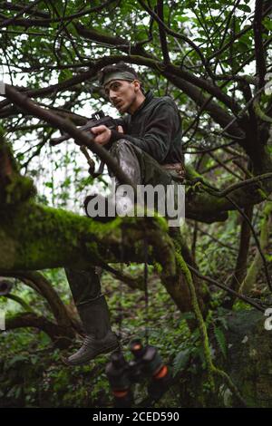 Soldat ou membre révolutionnaire ou chasseur en camouflage sur le arbre observant le canon dans sa main Banque D'Images