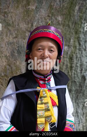 YUNNAN, CHINE - 14 JUIN 2018 : femme chinoise en costume traditionnel brillant pour une représentation musicale regardant un appareil photo et souriant debout sur un mur rocheux à Shilin?dans la province chinoise du Yunnan Banque D'Images