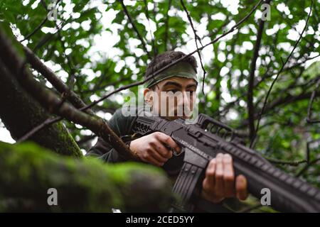 Soldat ou membre révolutionnaire ou chasseur en camouflage sur le arbre observant le canon dans sa main Banque D'Images