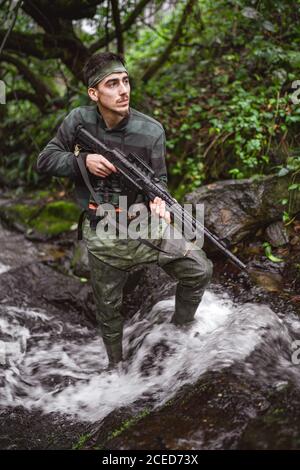 Soldat ou membre révolutionnaire ou chasseur en camouflage dans le flux observant le pistolet dans sa main Banque D'Images