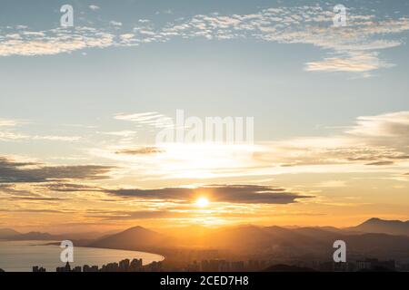 Coucher de soleil lumineux éclairant les montagnes et le paysage urbain côtier depuis un ciel nuageux, Sanya, province de Hainan, Chine Banque D'Images