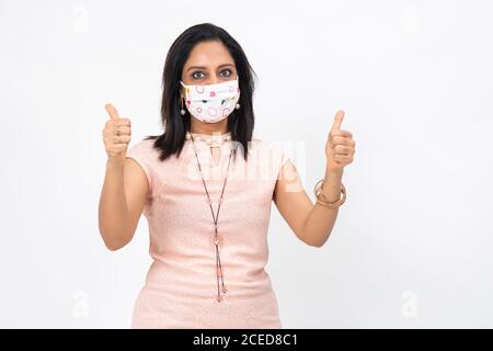 Jolie femme indienne portant un masque de protection Covid-19. Femme montrant ses pouces montrant le signe de la victoire et du succès. Banque D'Images