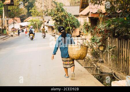 Vue arrière d'une femme asiatique adulte marchant sur la route dans le village et portant le panier. Banque D'Images