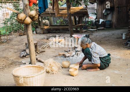 Vue latérale d'une femme asiatique senior assise et faisant des paniers. Banque D'Images