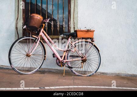 Vélo d'époque peint en rose et rouillé, garé à la fenêtre de la rue. Banque D'Images