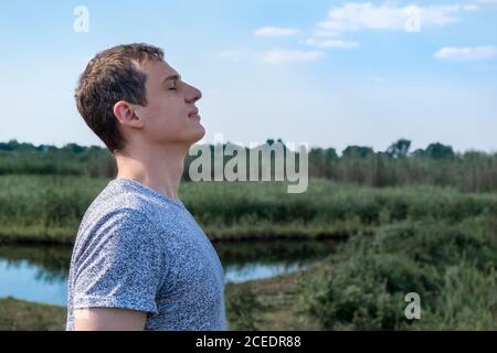 Homme adulte détendu respirant de l'air frais à l'extérieur avec le lac et champ en arrière-plan Banque D'Images