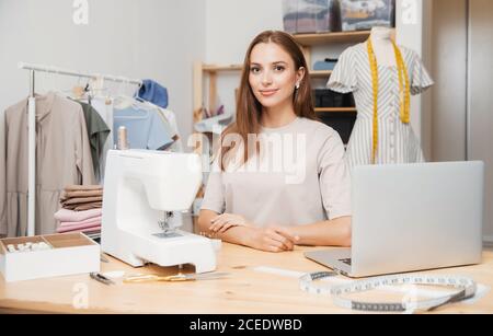 Belle jeune femme designer de mode assis lieu de travail de couturière, ordinateur portable, machine à coudre, mannequin Banque D'Images