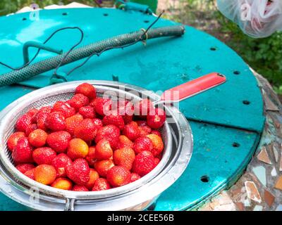 Un bol avec écumoire rempli de baies de fraises mûres fraîches sur un couvercle d'un puits à l'ancienne. Concept d'éco-alimentation saine. Banque D'Images