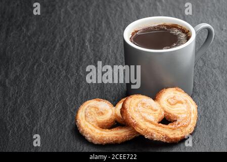 Cœur de pâte feuilletée émaillé de sucre caramélisé et d'une tasse de café sur fond de pierre noire Banque D'Images