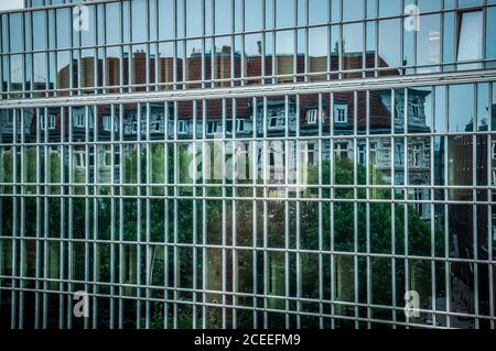 Mur de verre encadré d'un bâtiment d'entreprise à Hambourg en Allemagne. Reflet déformé du toit d'une maison ancienne dans une surface en miroir de l'architecture moderne Banque D'Images