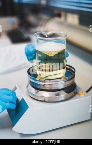 Vue rognée des mains de la personne avec des gants médicaux bleus placer la cupule doseuse avec du liquide jaune sur la balance en laboratoire Banque D'Images