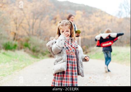 Petite fille touchant son nez et souriant avec sa famille en arrière-plan Banque D'Images