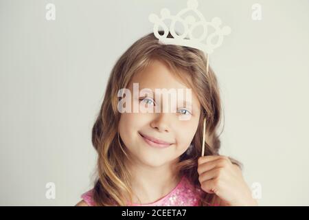 Portrait d'une jolie petite fille avec couronne en papier blanc sur fond blanc Banque D'Images