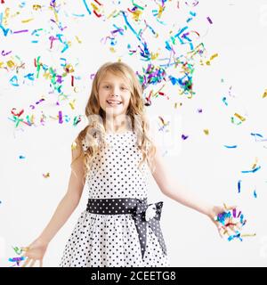 Petite fille sautant et s'amusant célébrant l'anniversaire. Portrait d'un enfant jette plusieurs couleurs scintillant et confetti. Émotions positives. Heureux sauf Banque D'Images