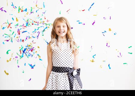 Petite fille sautant et s'amusant célébrant l'anniversaire. Portrait d'un enfant jette plusieurs couleurs scintillant et confetti. Émotions positives. Heureux sauf Banque D'Images