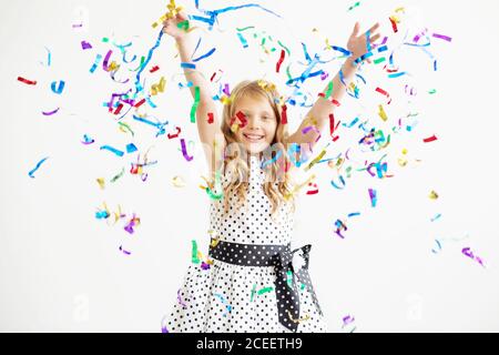 Petite fille sautant et s'amusant célébrant l'anniversaire. Portrait d'un enfant jette plusieurs couleurs scintillant et confetti. Émotions positives. Heureux sauf Banque D'Images