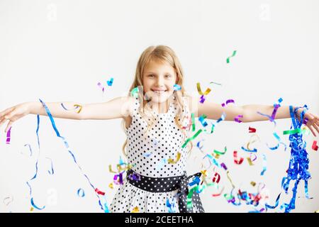 Petite fille sautant et s'amusant célébrant l'anniversaire. Portrait d'un enfant jette plusieurs couleurs scintillant et confetti. Émotions positives. Heureux sauf Banque D'Images