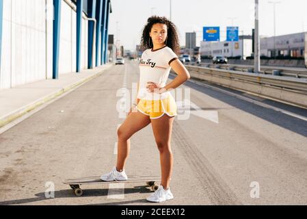 Adolescent afro-américain avec planche à roulettes debout sur la route Banque D'Images