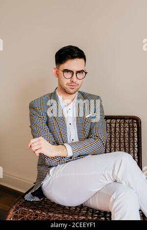 Jeune homme pensif dans une veste élégante et décontractée, assis sur une chaise et regardant l'appareil photo. Banque D'Images