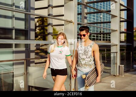 Jeune couple marchant tenant les mains et portant le skateboard Banque D'Images