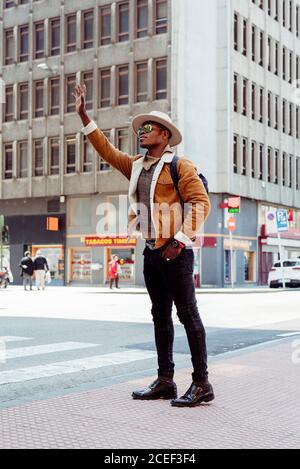 Jeune homme africain en chapeau et lunettes debout dans la rue et essayez de prendre un taxi Banque D'Images