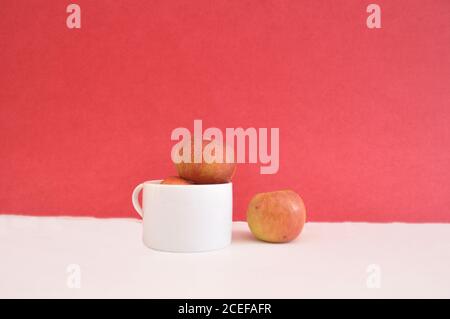Pommes dans une tasse blanche avec une pomme isolée concept de séparation d'arrière-plan rouge Banque D'Images